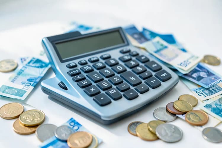 Uma calculadora com notas de dinheiro e moedas ao lado, representando cálculo de custos.