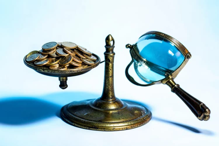 Uma balança com moedas de um lado e uma lupa do outro, representando análise de custos.