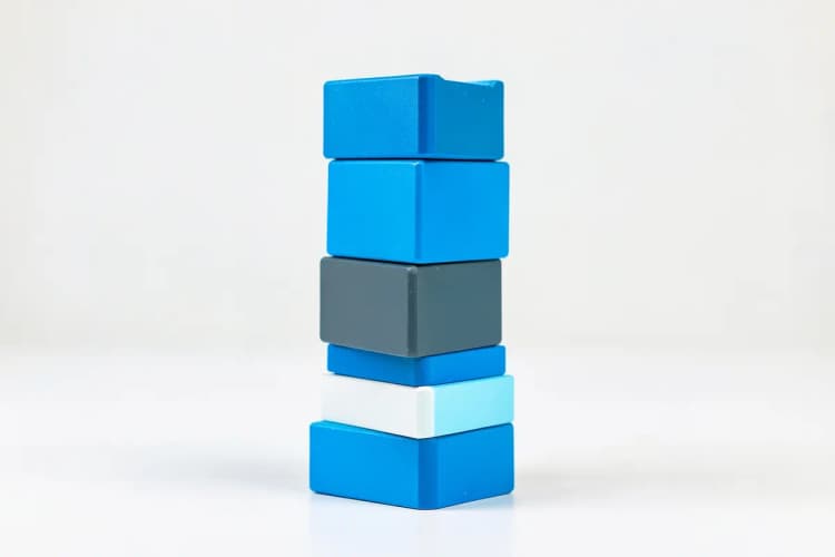 Uma pilha de blocos de construção coloridos, formando uma torre instável. A iluminação é difusa e uniforme, vindo de todos os lados, sem sombras fortes. A imagem é um plano médio, mostrando a estrutura da torre e a textura dos blocos.