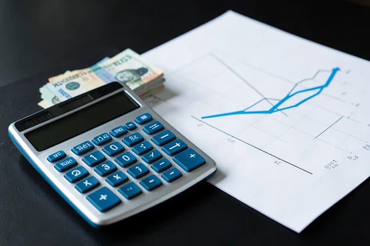 Calculadora ao lado de notas de dinheiro e um gráfico de linha ascendente.