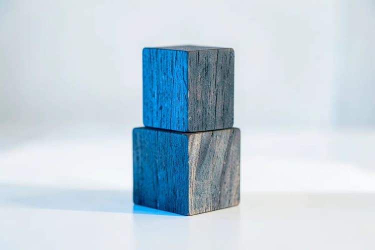 Três cubos de madeira empilhados em forma de pirâmide sobre uma superfície clara.