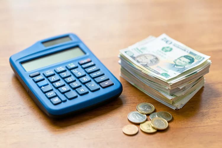 Uma calculadora ao lado de notas de dinheiro e moedas em uma superfície de madeira.