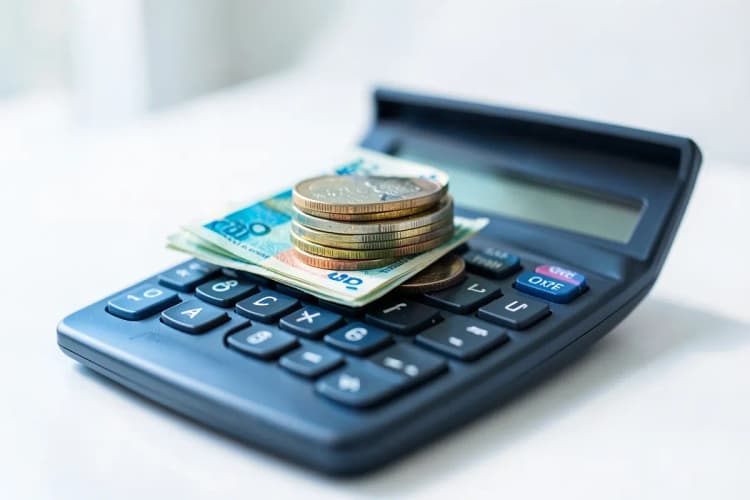 Moedas empilhadas e notas de dinheiro em cima de uma calculadora, simbolizando o custo da gestão de tráfego pago.
