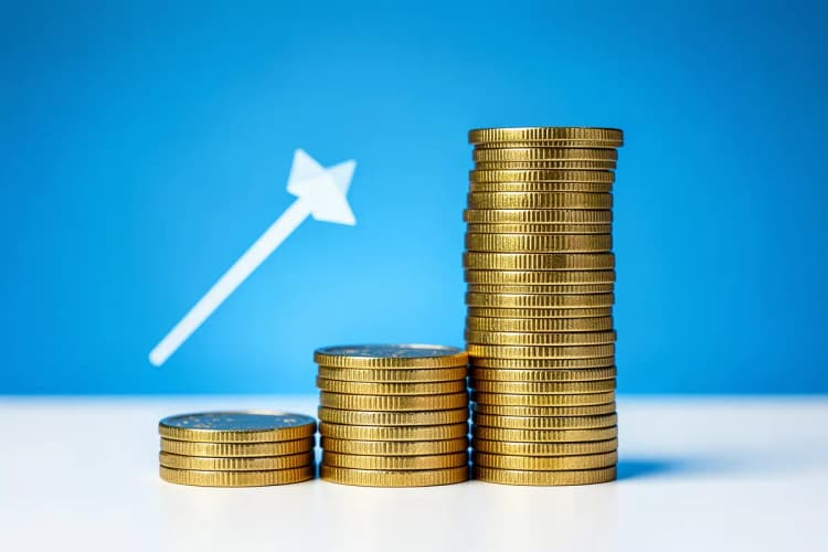 Três pilhas de moedas de ouro de tamanhos diferentes, com uma seta apontando para cima ao lado da maior pilha, em um fundo gradiente azul.