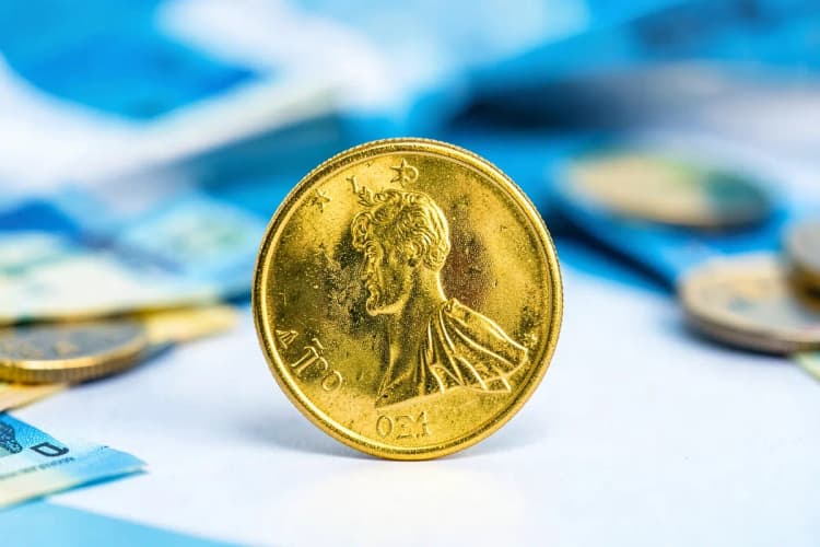 Uma única moeda de ouro brilhante em destaque, com um fundo desfocado de notas de dinheiro e outras moedas.