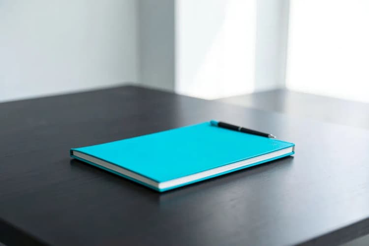 Um notebook fechado e uma caneta sobre uma mesa de madeira escura, com foco suave.