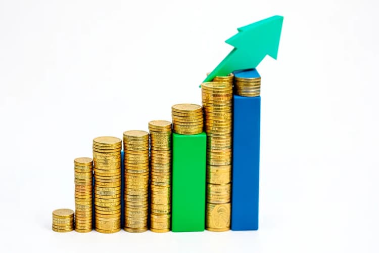 Gráfico de barras ascendente feito de moedas de ouro e notas de dinheiro, com uma seta verde apontando para cima.
