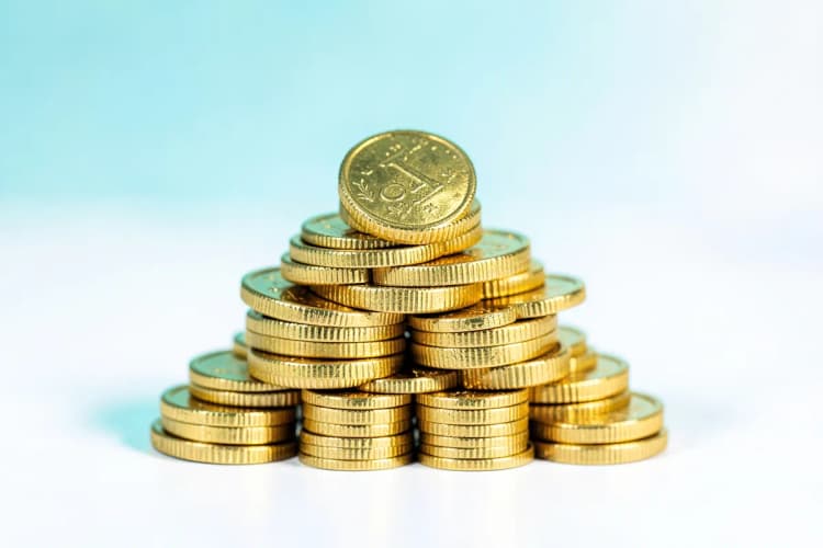 Moedas de dinheiro empilhadas formando uma pirâmide, em fundo branco.