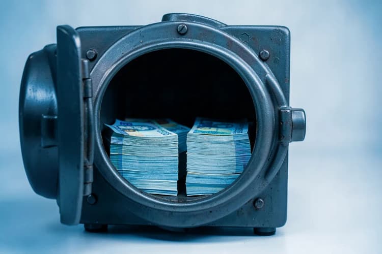 Um cofre de banco aberto com várias pilhas de notas de dinheiro dentro.